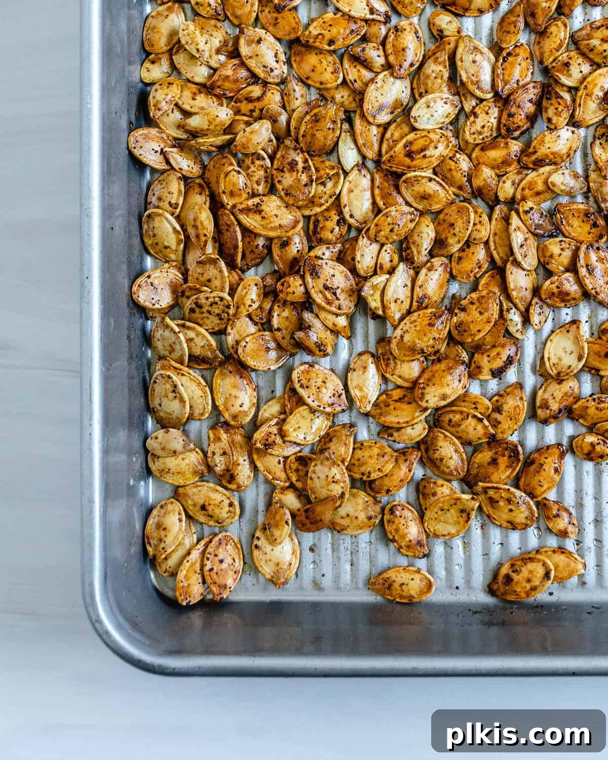 Fiery Roasted Pumpkin Seeds 2 Crispy, golden-brown roasted spicy pumpkin seeds seasoned with soy sauce, garlic, and cayenne, spread on a baking tray.