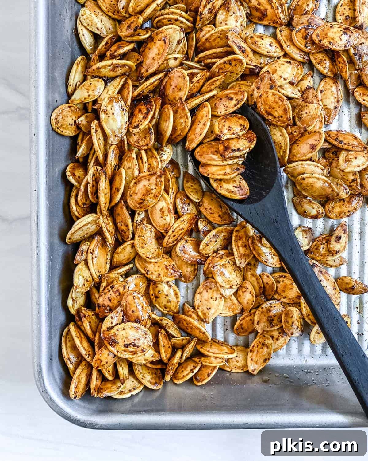 Fiery Roasted Pumpkin Seeds 7 Freshly roasted spicy pumpkin seeds being mixed on a baking tray, showcasing their golden-brown color and crispy texture.