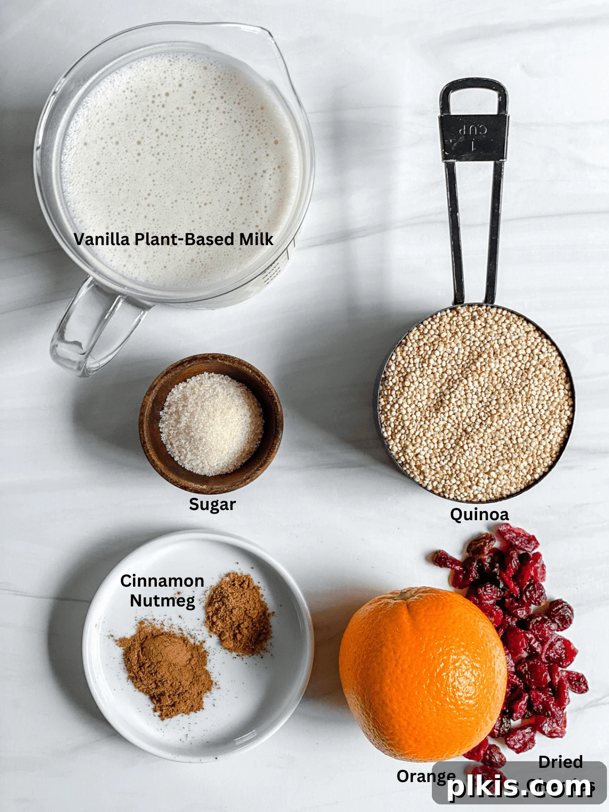Spiced Orange Quinoa 3 Individual ingredients for Cinnamon Orange Quinoa, including quinoa, plant-based milk, fresh oranges, cinnamon, nutmeg, and dried fruits, neatly arranged on a white surface.