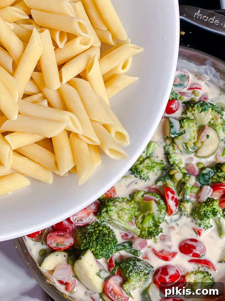 Vibrant Vegan Primavera Pasta 11 Cooked pasta being added to a pot containing vegetables and cream sauce.