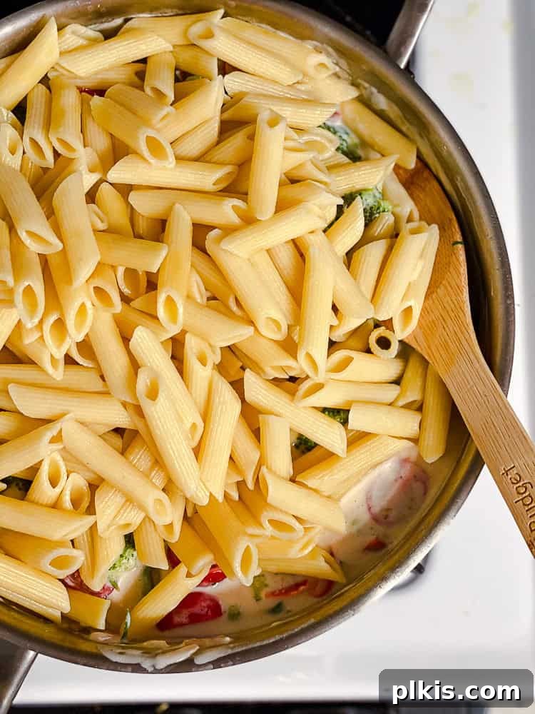Vibrant Vegan Primavera Pasta 12 A wooden spoon tossing cooked pasta, vegetables, and creamy sauce in a large pot, ensuring all ingredients are combined.