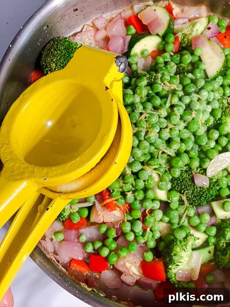 Vibrant Vegan Primavera Pasta 7 A hand squeezing lemon juice into a pot filled with cooking vegetables and herbs.