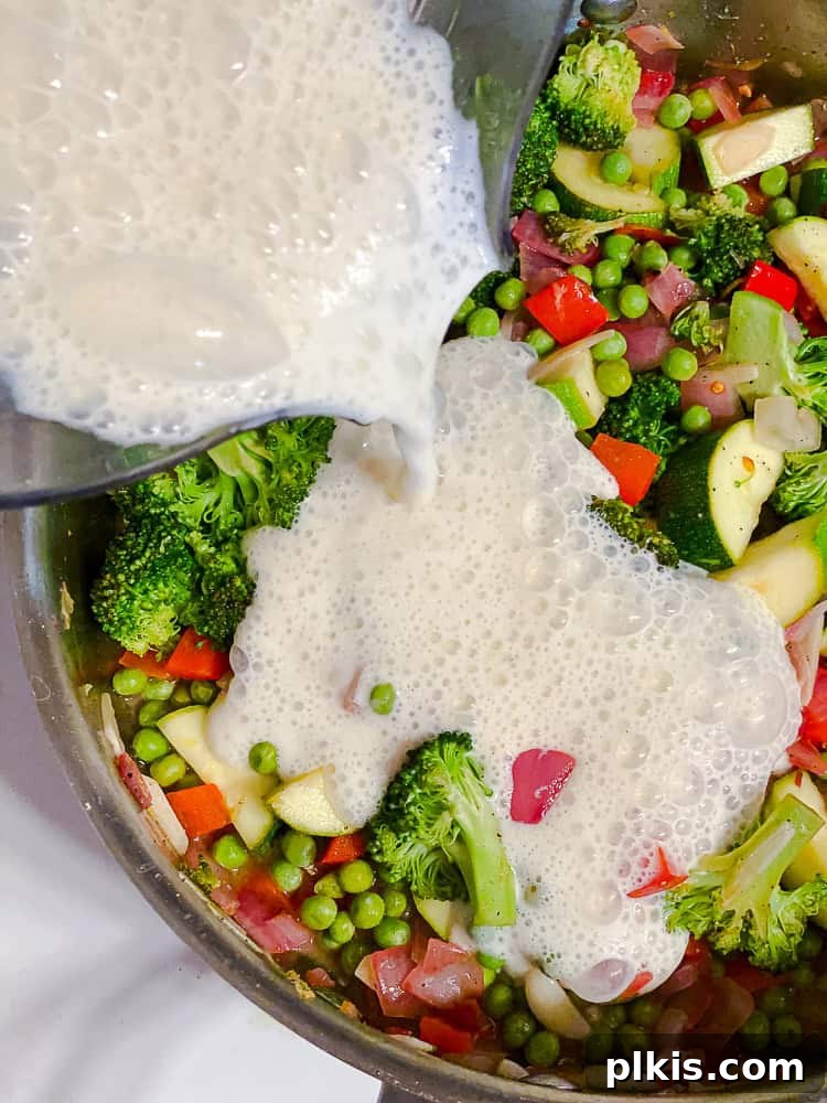 Vibrant Vegan Primavera Pasta 10 Creamy silken tofu sauce being poured into a pot of cooked vegetables.