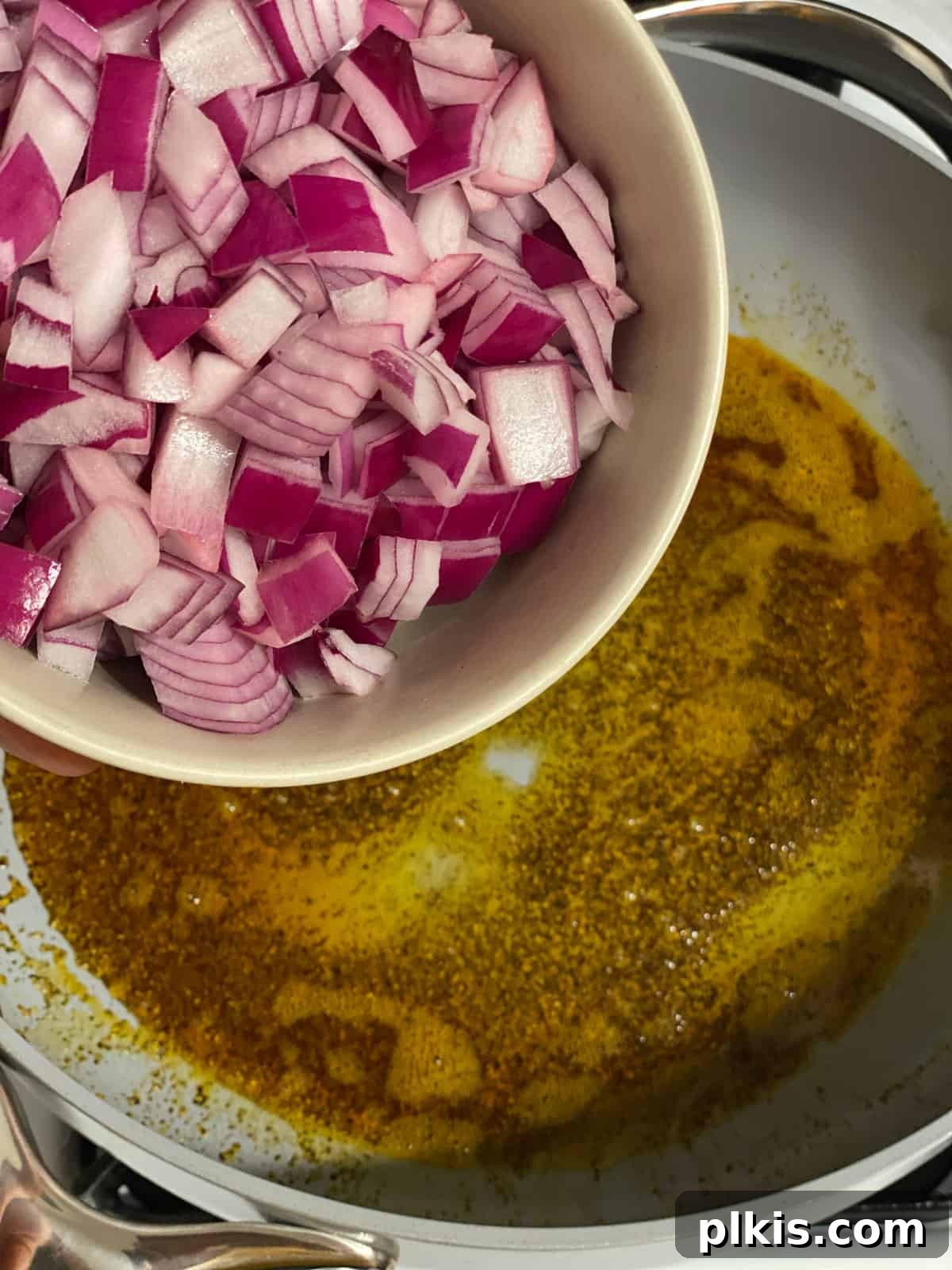 One-Pan Roasted Root Vegetable Medley 5 Process shot showing diced onions being added to the skillet with hot oil and paprika.