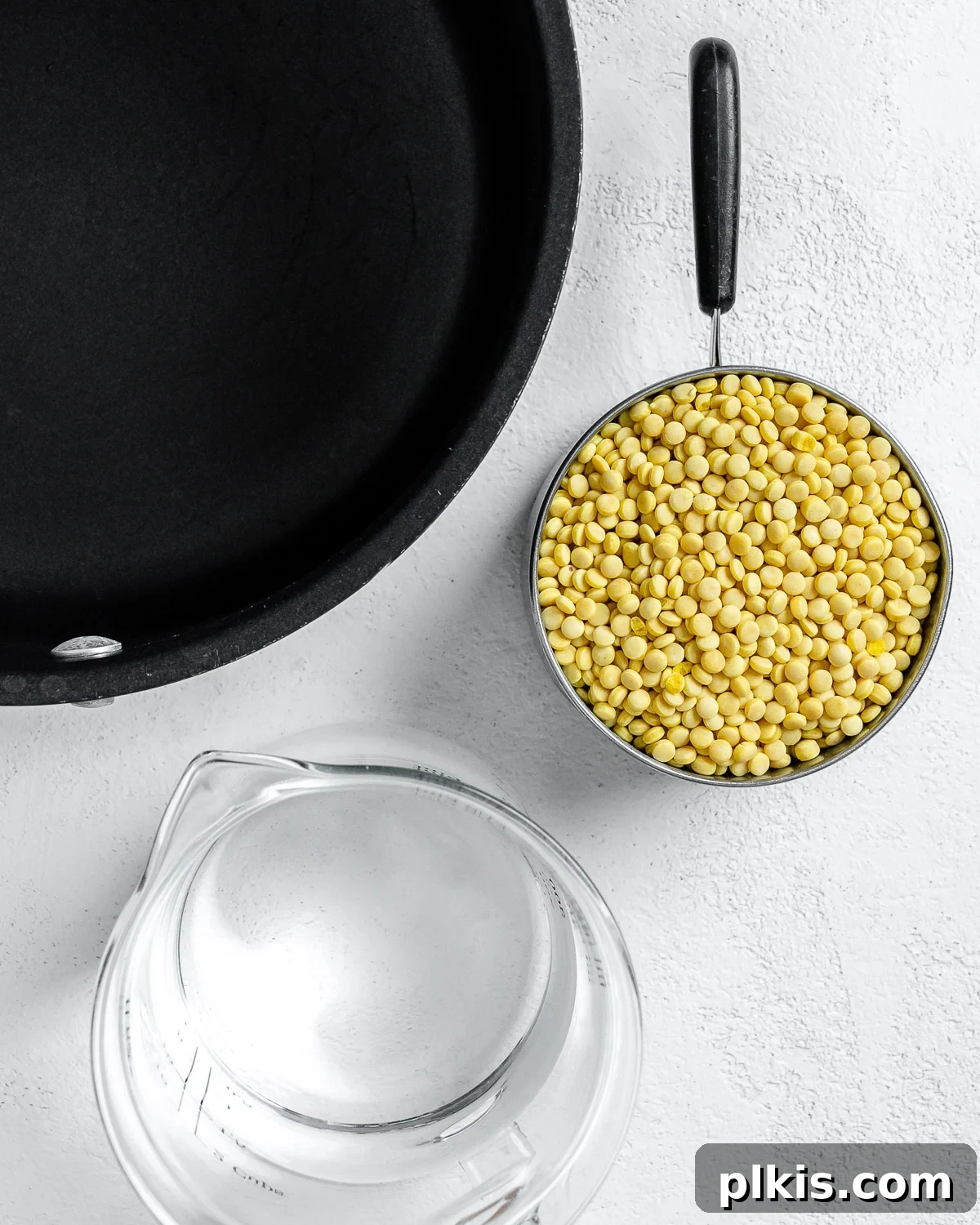 Vibrant Vegan Couscous with Fresh Vegetables 4 Skillet alongside water and couscous against a white surface, illustrating the first step of cooking couscous