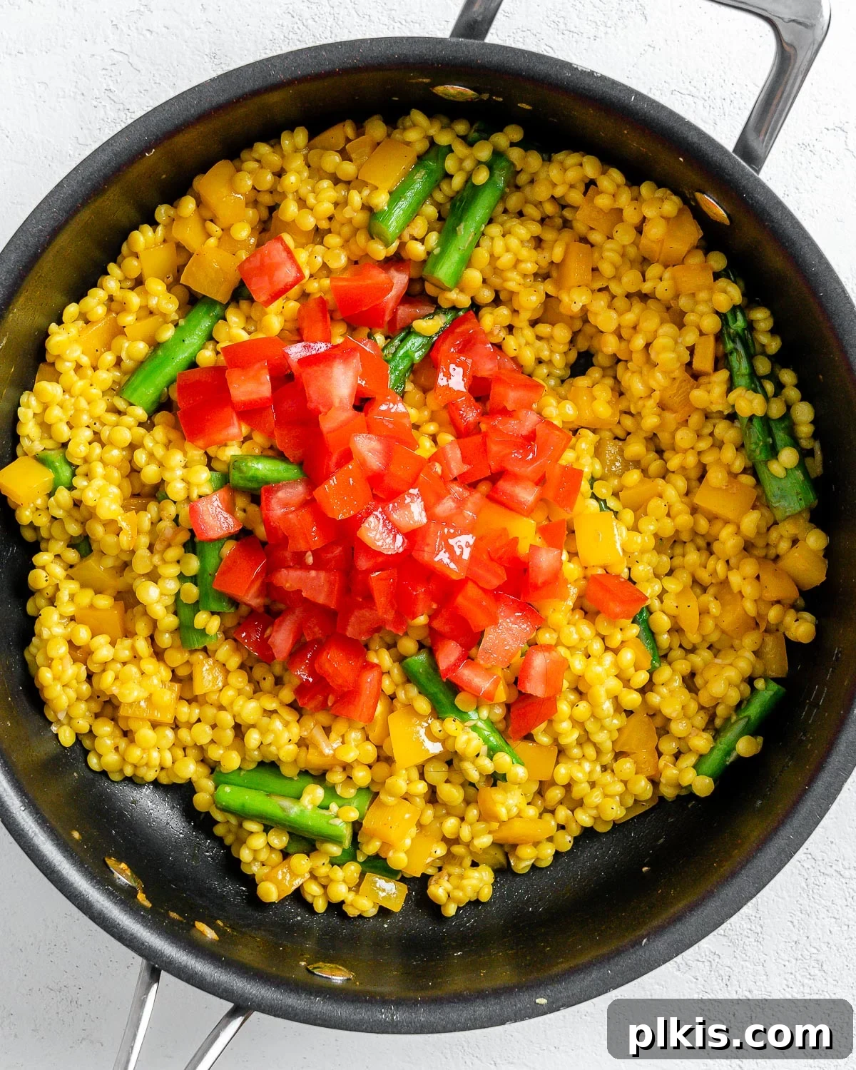 Vibrant Vegan Couscous with Fresh Vegetables 7 Process of adding fresh diced tomatoes to the couscous and veggie mix in a pan, for final combining
