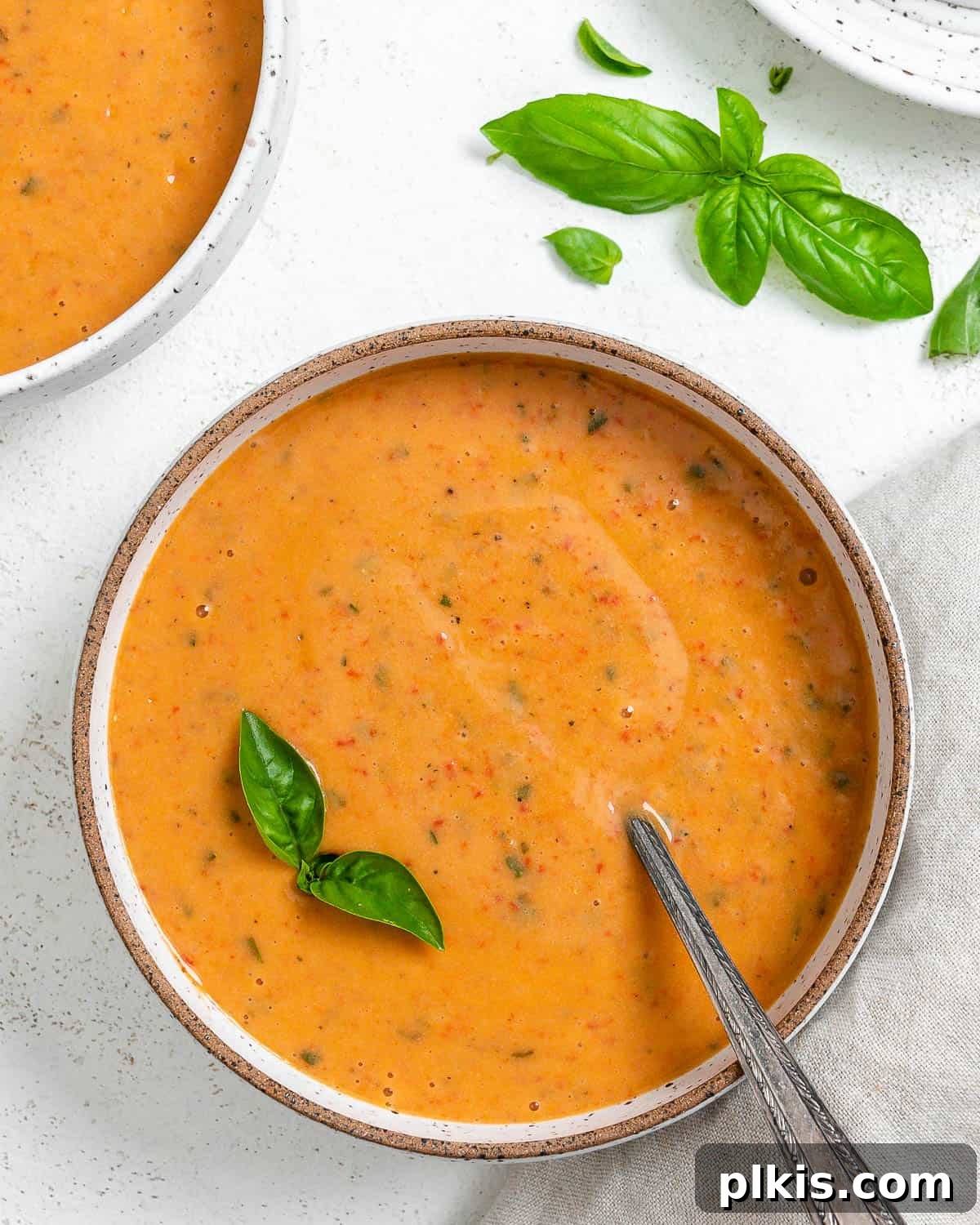Velvety Roasted Red Pepper Soup 2 Two bowls of creamy roasted red pepper soup garnished with fresh basil, against a light backdrop.