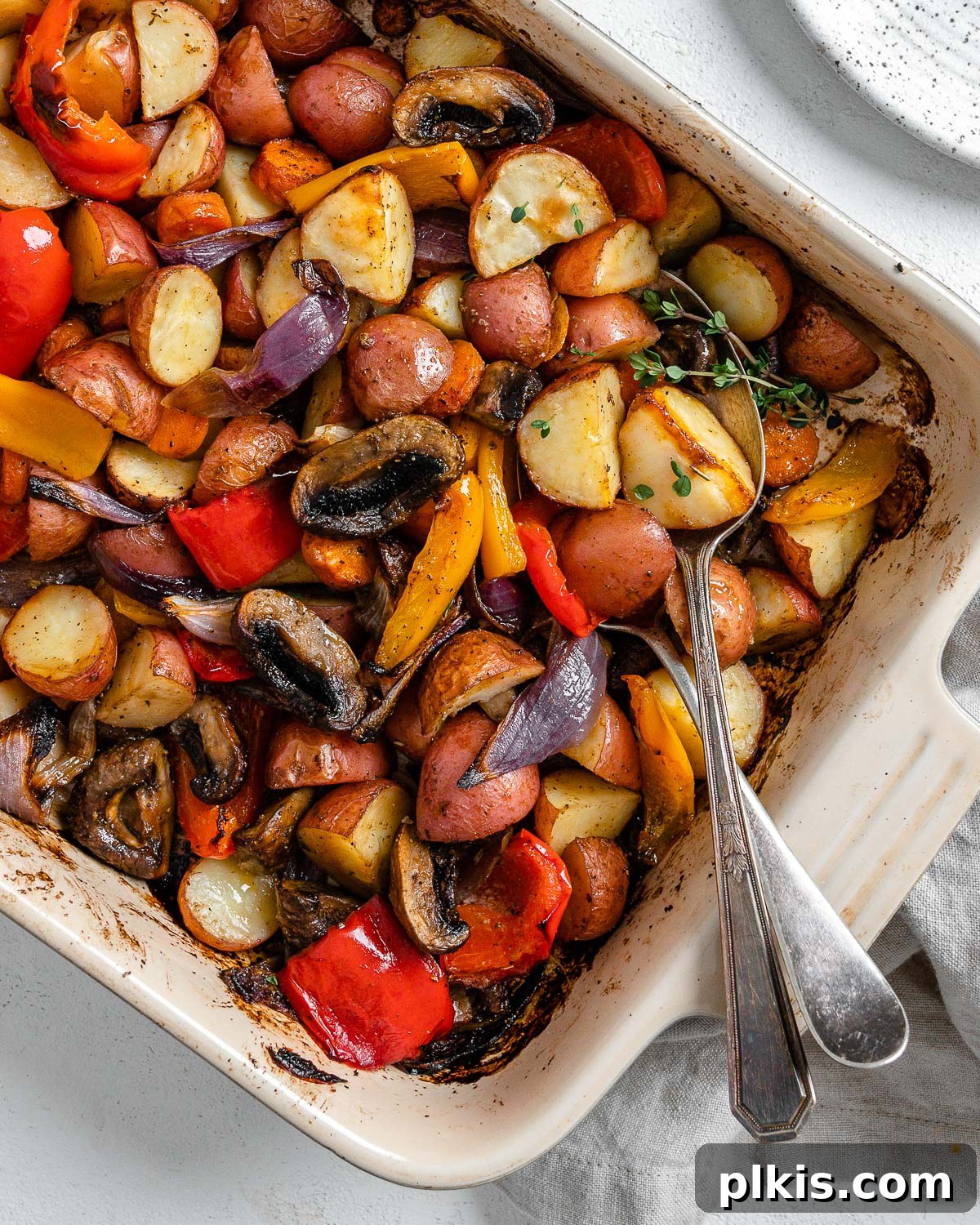 Thyme Kissed Roasted Vegan Medley 2 Completed Vegan Roasted Vegetables with Thyme in a baking dish against a white background, garnished with fresh thyme.