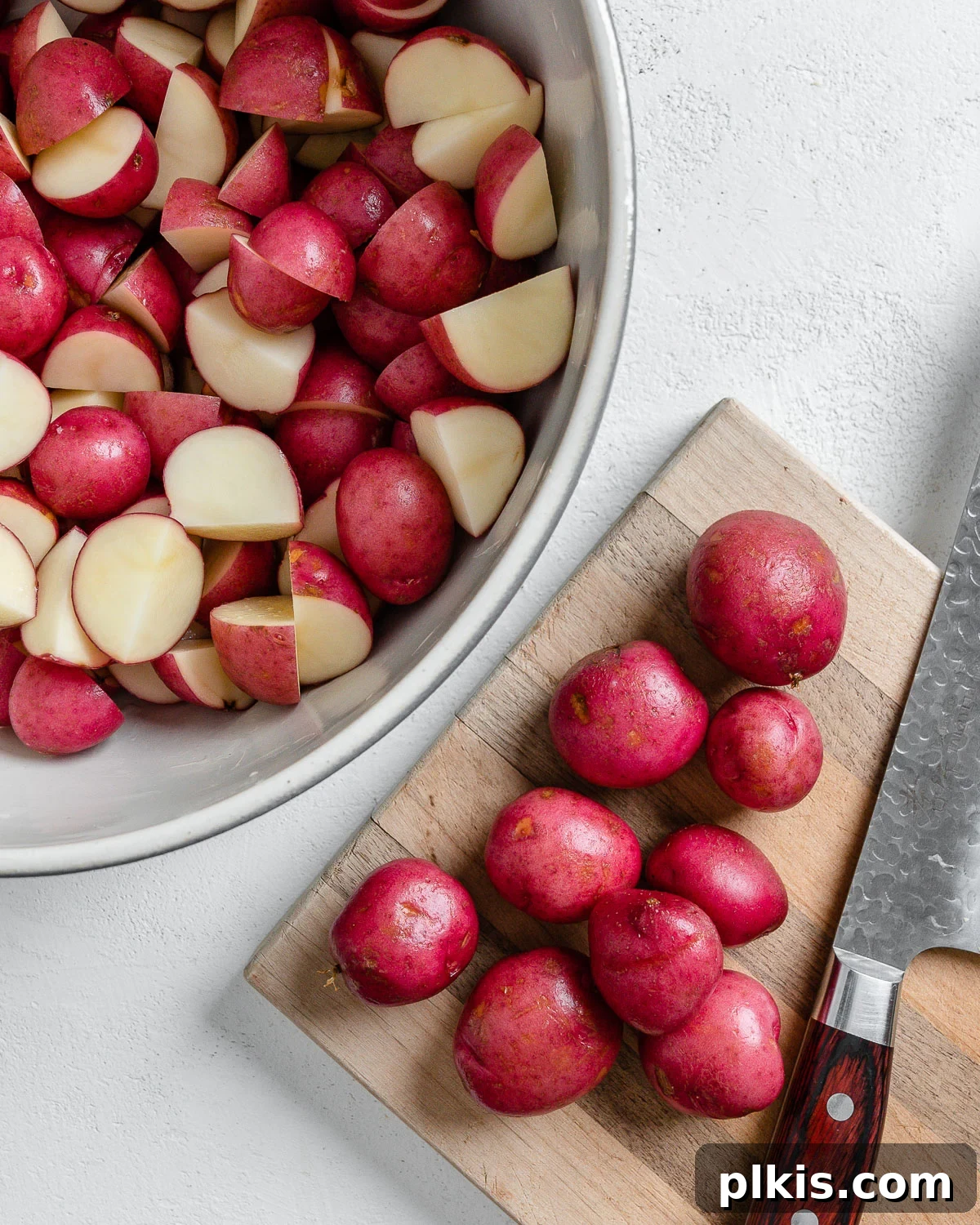 Thyme Kissed Roasted Vegan Medley 4 Process of cutting red potatoes into cubes on a brown cutting board, with some cut potatoes already in a bowl.