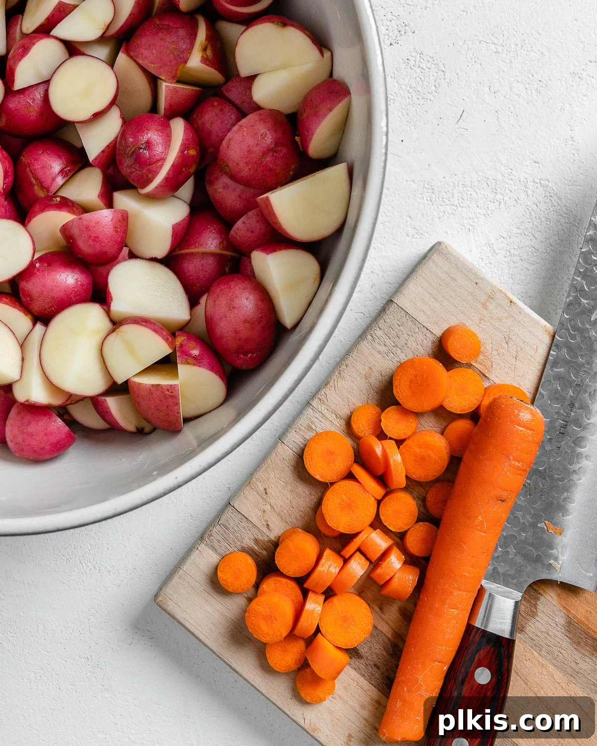 Thyme Kissed Roasted Vegan Medley 5 Process of slicing carrots on a brown cutting board, next to a bowl of pre-cut potatoes.