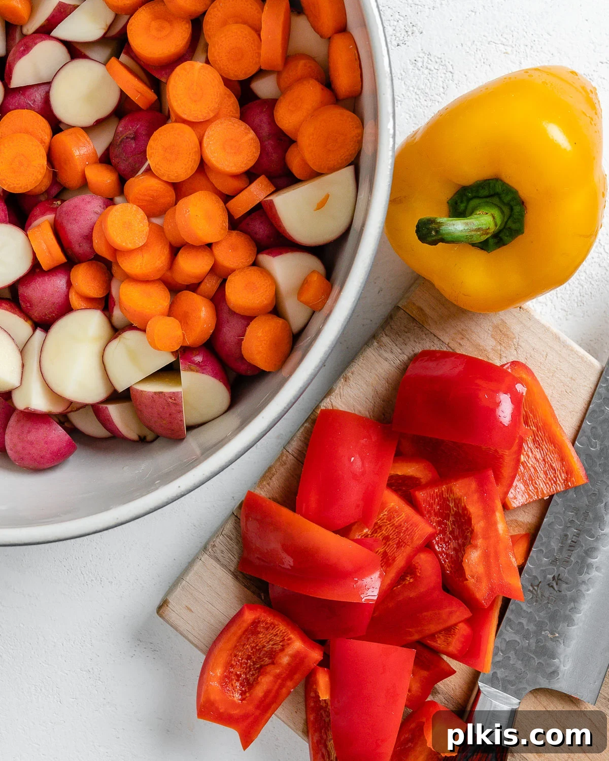 Thyme Kissed Roasted Vegan Medley 6 Process of cutting colorful bell peppers on a cutting board, alongside a bowl of mixed potatoes and carrots.
