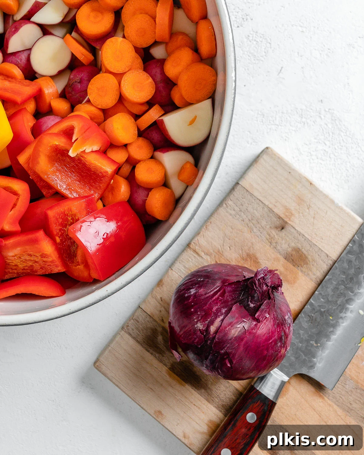 Thyme Kissed Roasted Vegan Medley 7 A whole red onion on a cutting board, ready for slicing, next to a bowl filled with prepped vegetables.