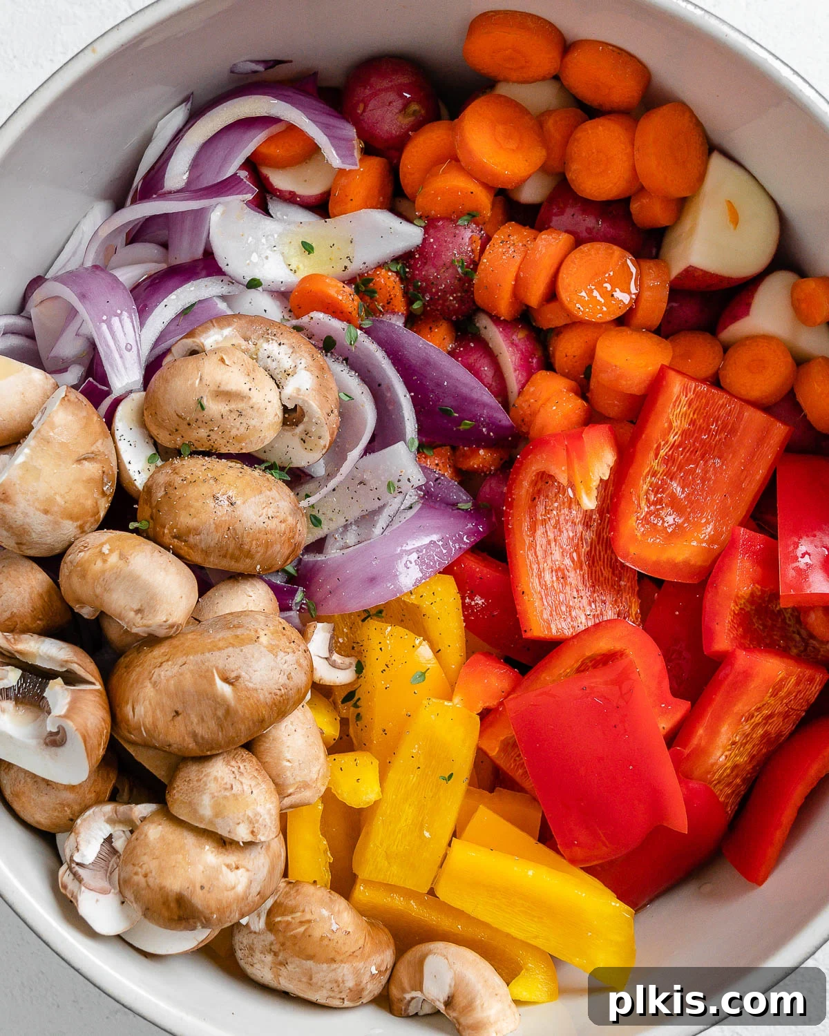 Thyme Kissed Roasted Vegan Medley 10 Process of adding dried thyme and other spices to the large bowl of mixed, cut vegetables, ready for tossing.