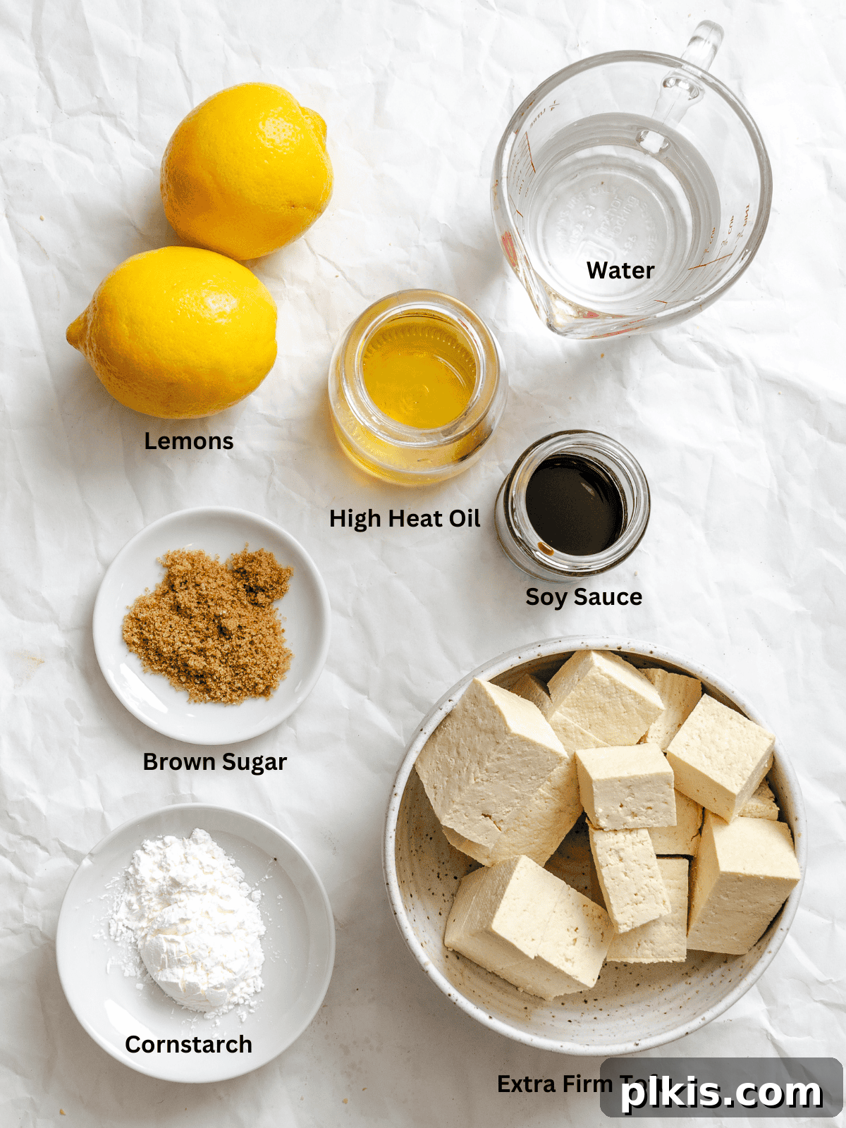 Zesty Lemon Glazed Tofu 3 Ingredients for Sticky Lemon Tofu measured out on a white surface, including soy sauce, brown sugar, lemons, water, cornstarch, oil, and a block of tofu.
