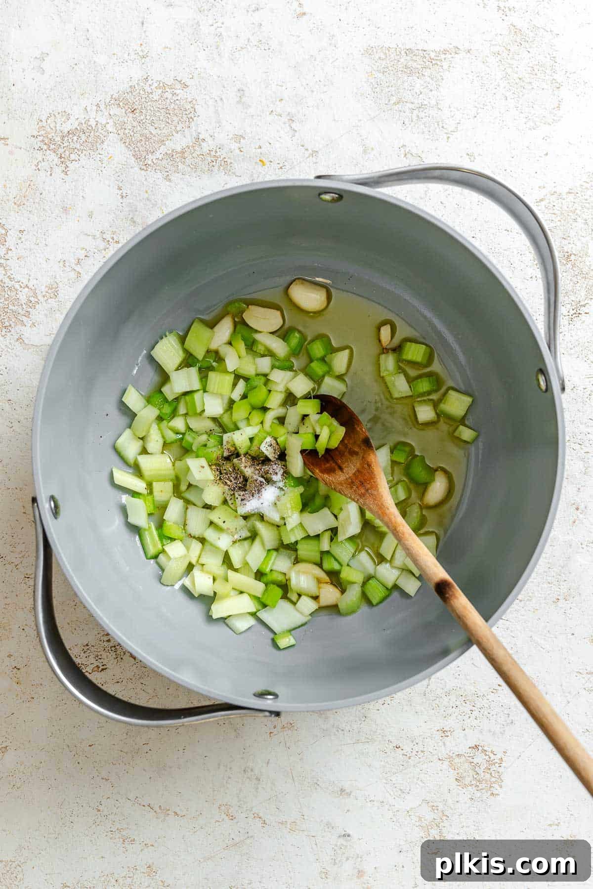 Velvety Celery Soup 4 Process shot showing mixing ingredients in a pan, including chopped celery and garlic.