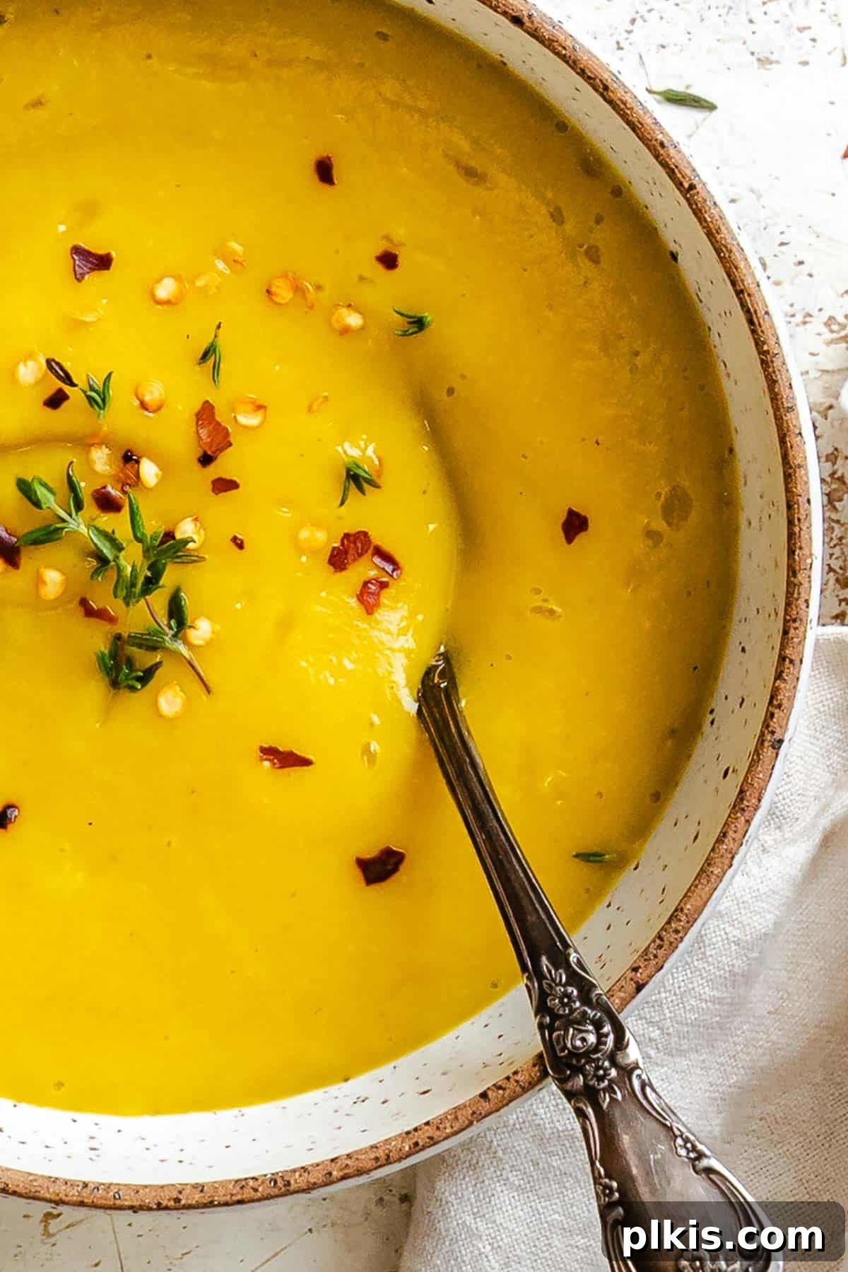 Velvety Golden Kabocha Soup 2 Completed Kabocha Squash Soup in a rustic ceramic bowl, garnished with fresh herbs, against a warm, inviting background, perfect for a cozy fall or winter meal.