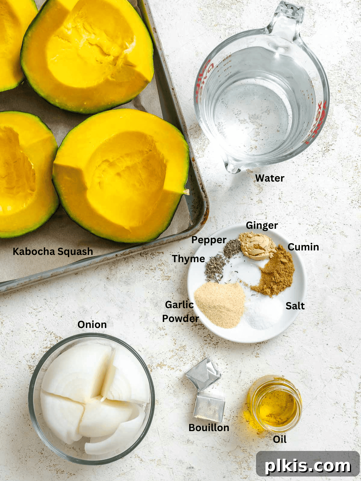 Velvety Golden Kabocha Soup 3 Fresh ingredients for Kabocha Squash Soup, including a whole kabocha squash, a yellow onion, a head of garlic, fresh ginger, and an array of spices, neatly arranged on a white surface.