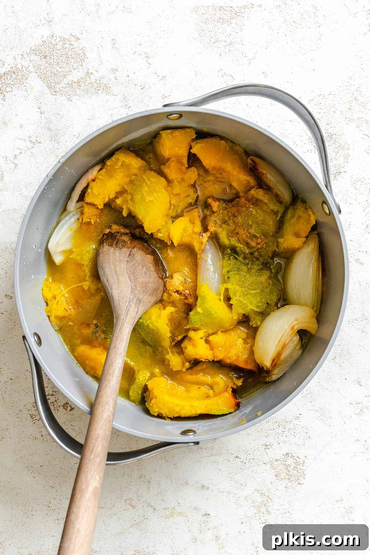 Velvety Golden Kabocha Soup 6 Process shot showing the roasted kabocha squash and onion being added to a large pot, along with various spices, ready for simmering.